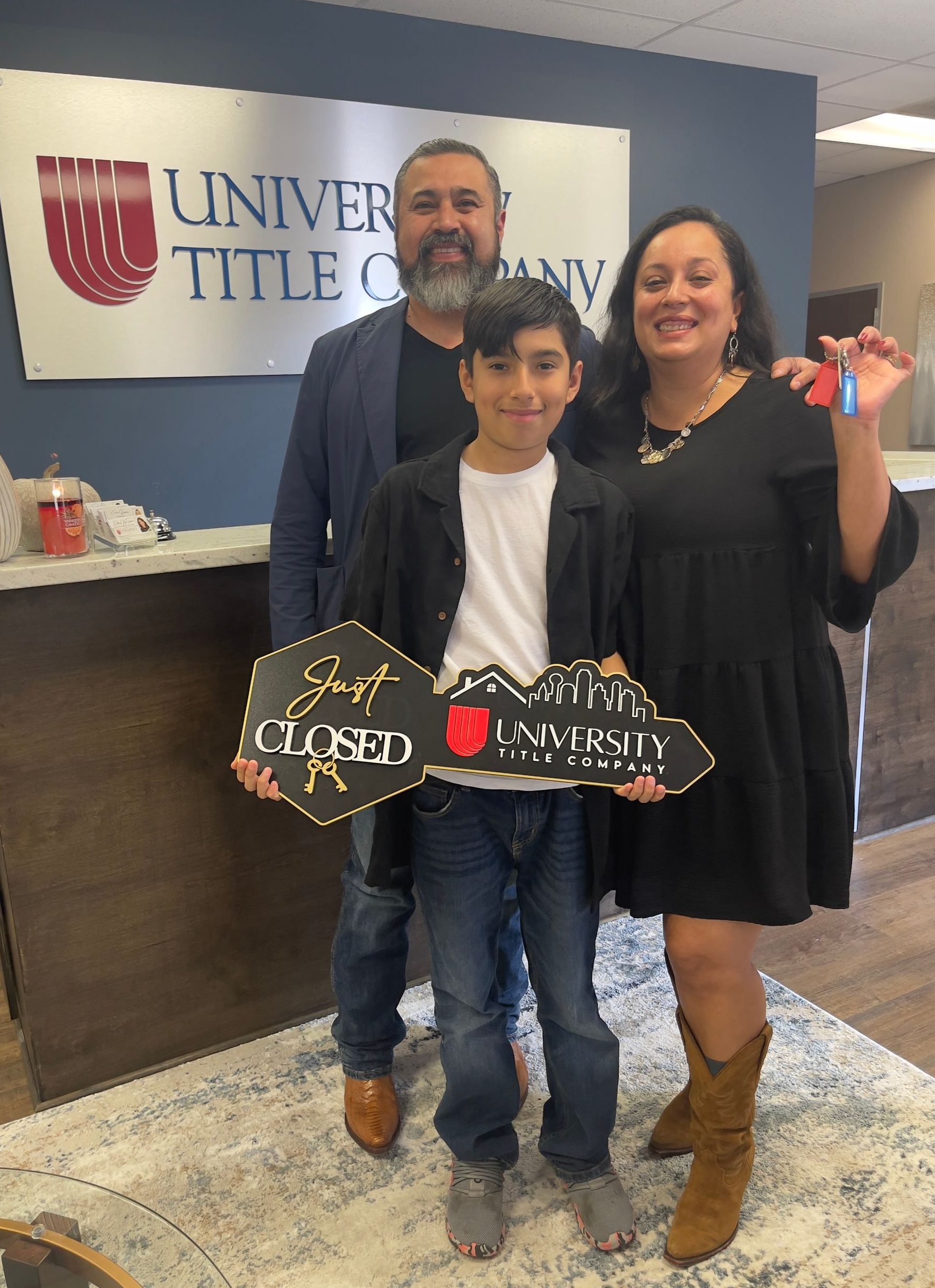 Family of three smiling, holding house key and keys in a title company.