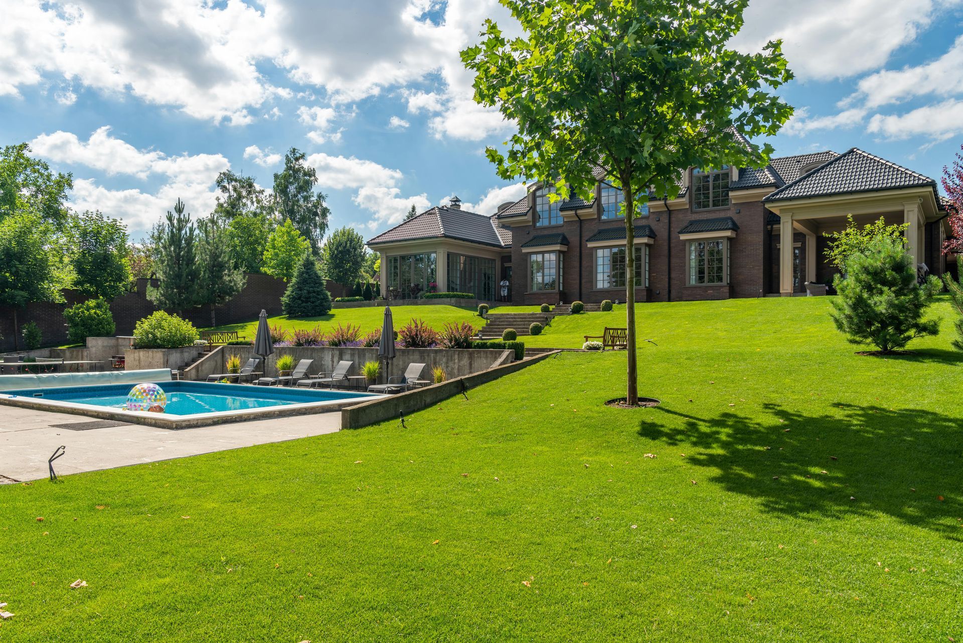 Luxurious house with a pool and green lawn under a partly cloudy sky.