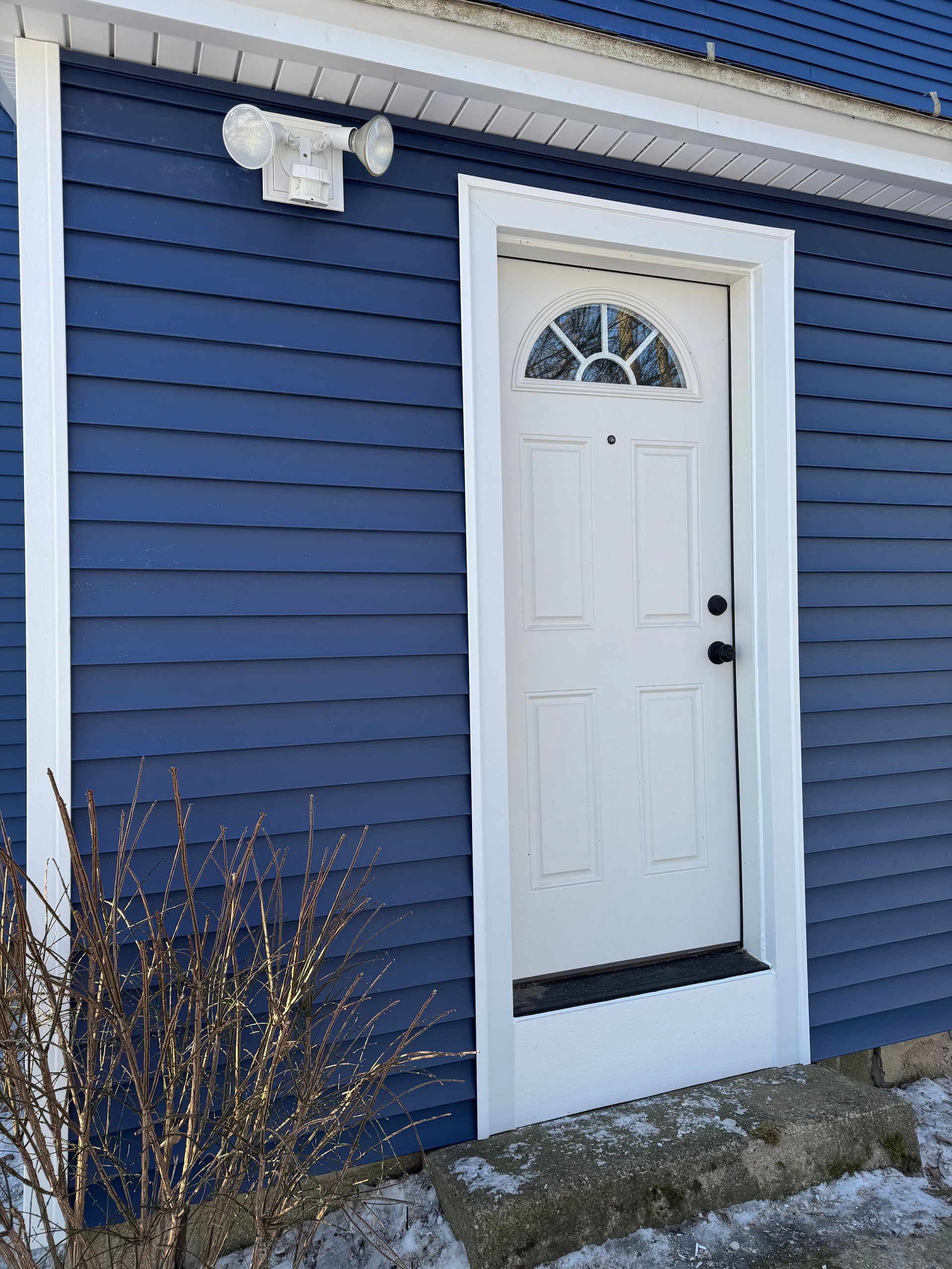 Blue house exterior with white door and trim, security lights above.