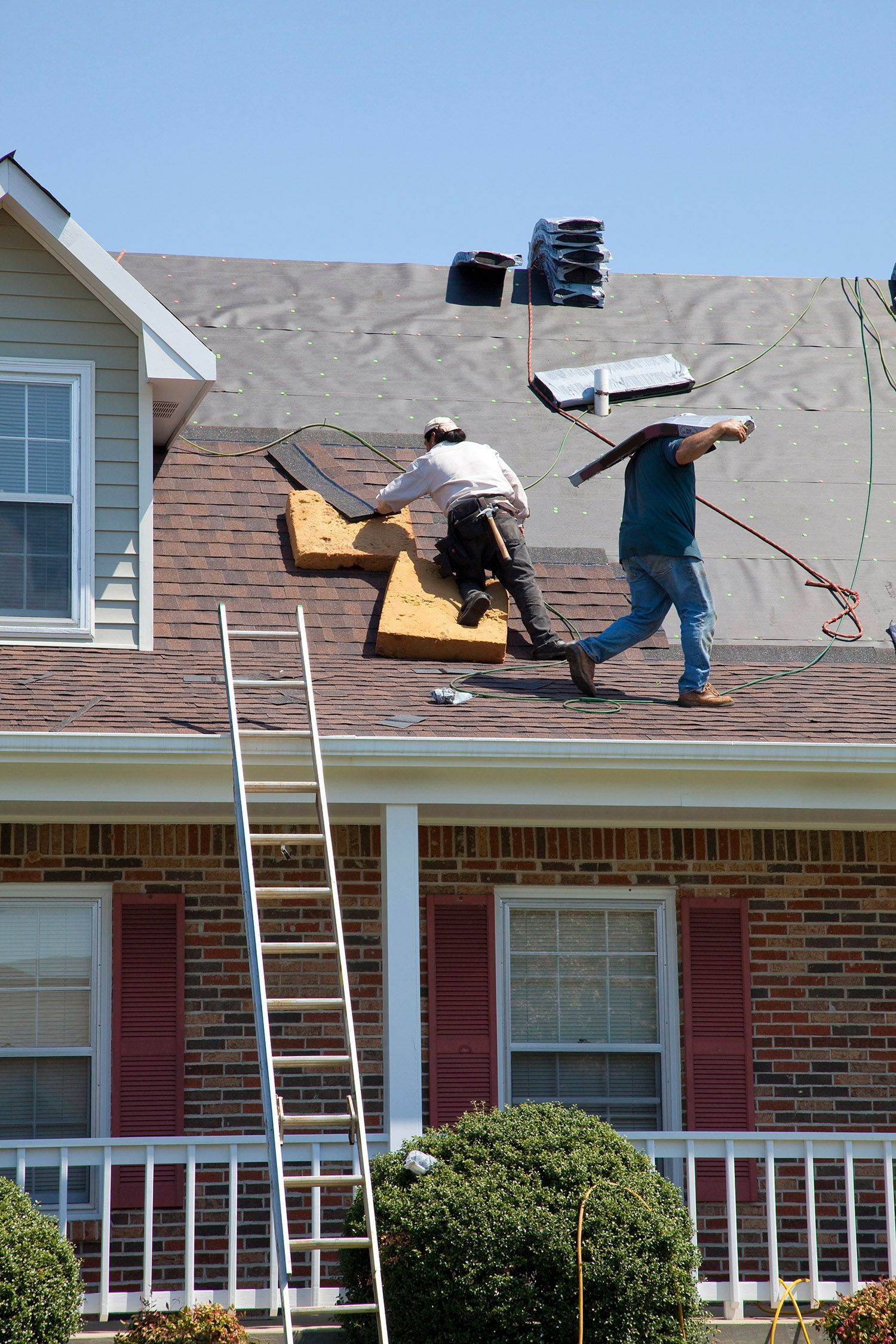 A pair of roofers install new shingles on the roof of a house, under the sun. A pair of roofers install new shingles on the roof of a house, under the sun.