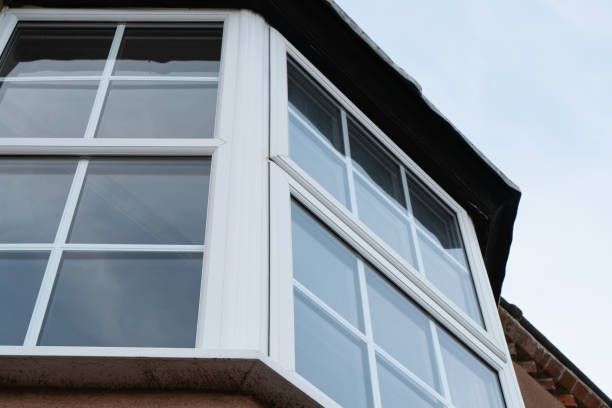 Bay window with white frames, set against a light blue sky. The window is part of a brown brick building.