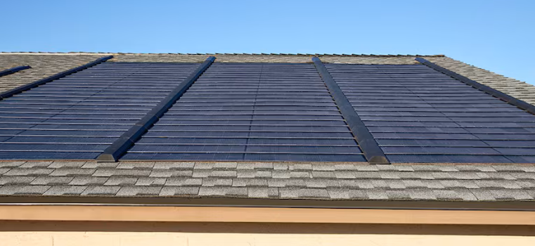 Solar panels on a shingled roof under a clear, blue sky.