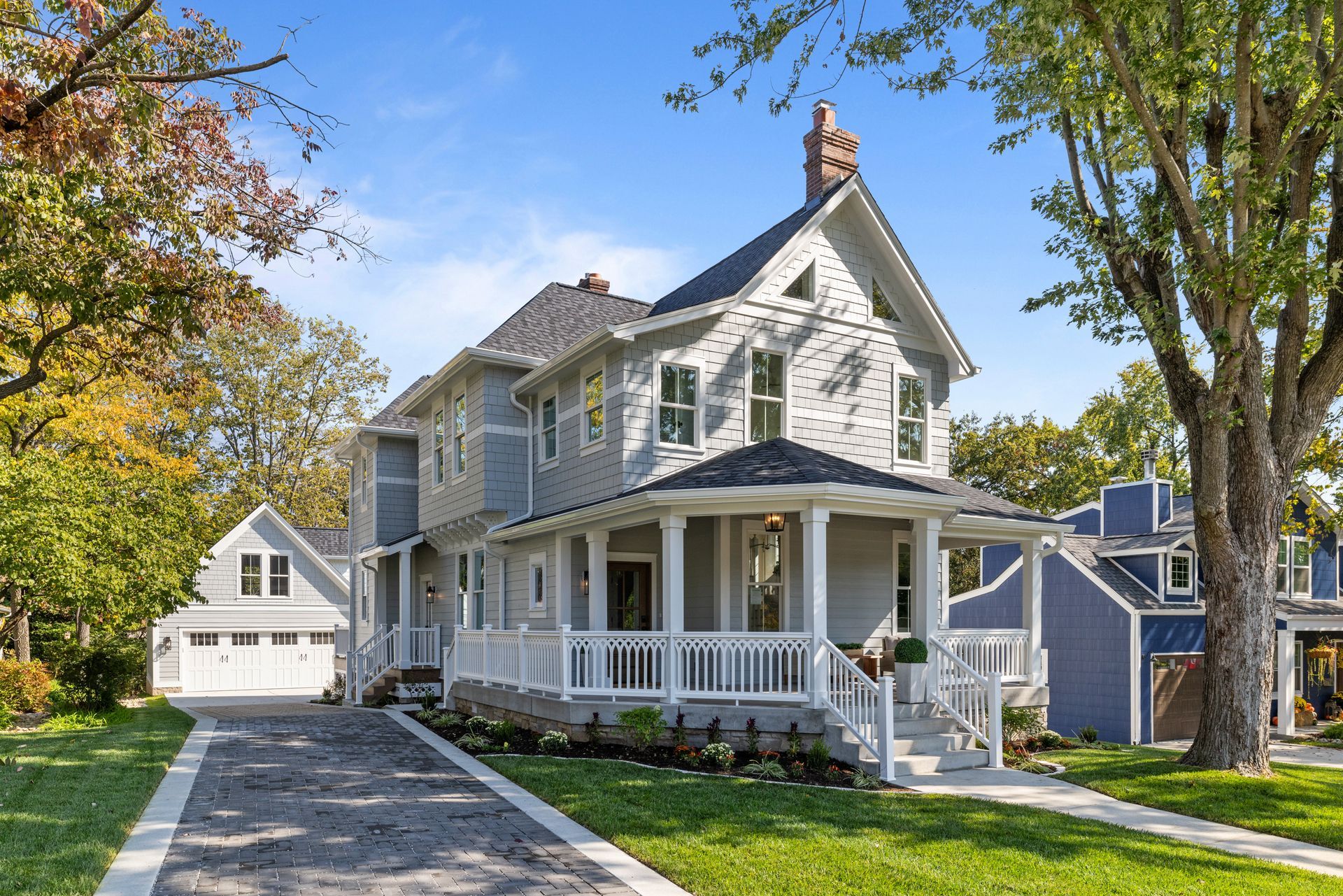 Gray house with porch, driveway, and detached garage on a sunny day.
