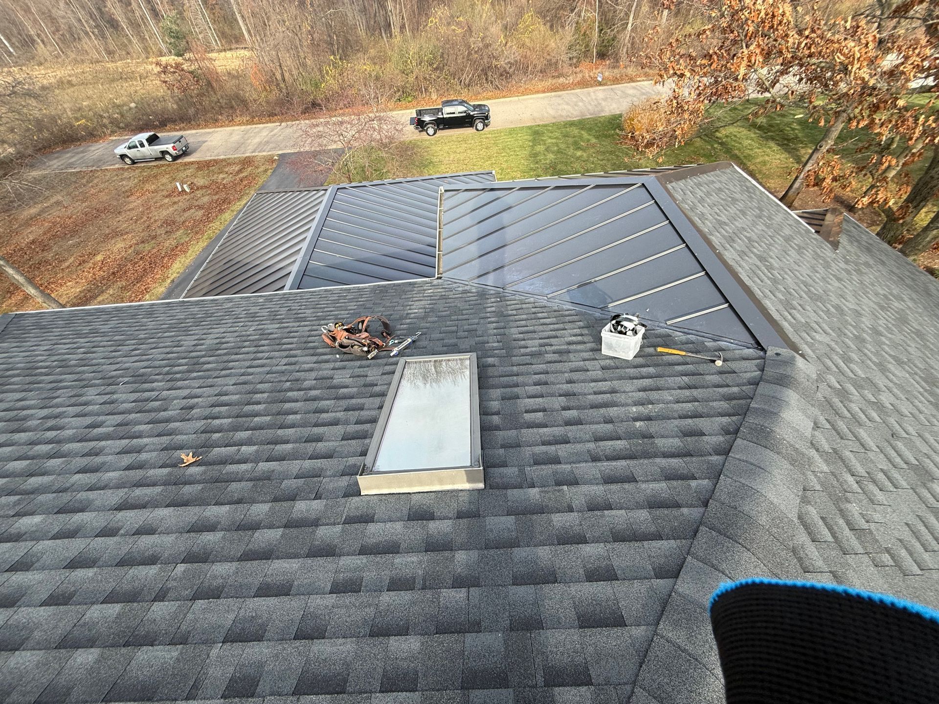 View from a rooftop: shingles, skylight, and a gray structure with a road and cars in the background.