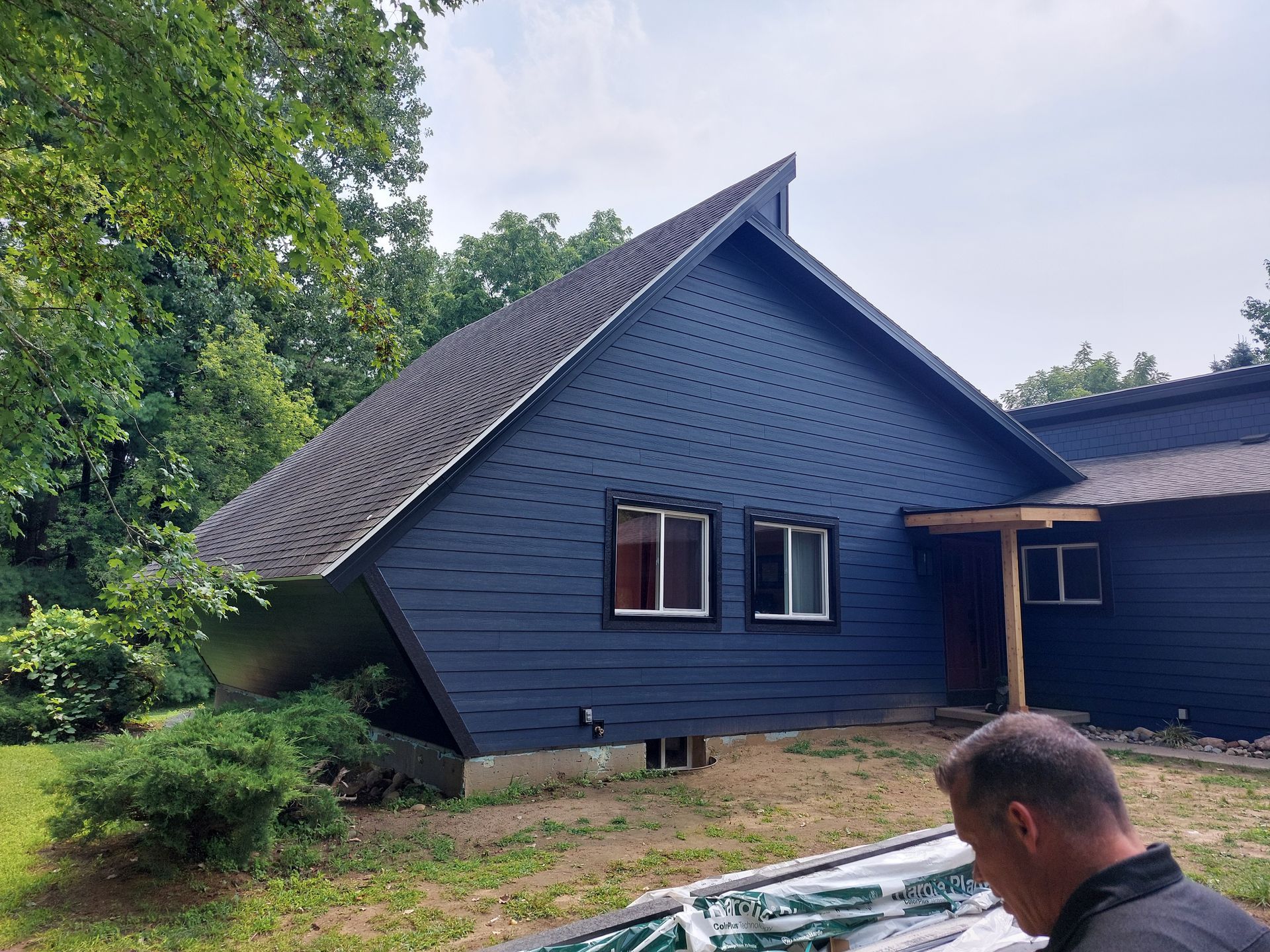 Dark blue house with angled roof and two windows. A man stands in front.