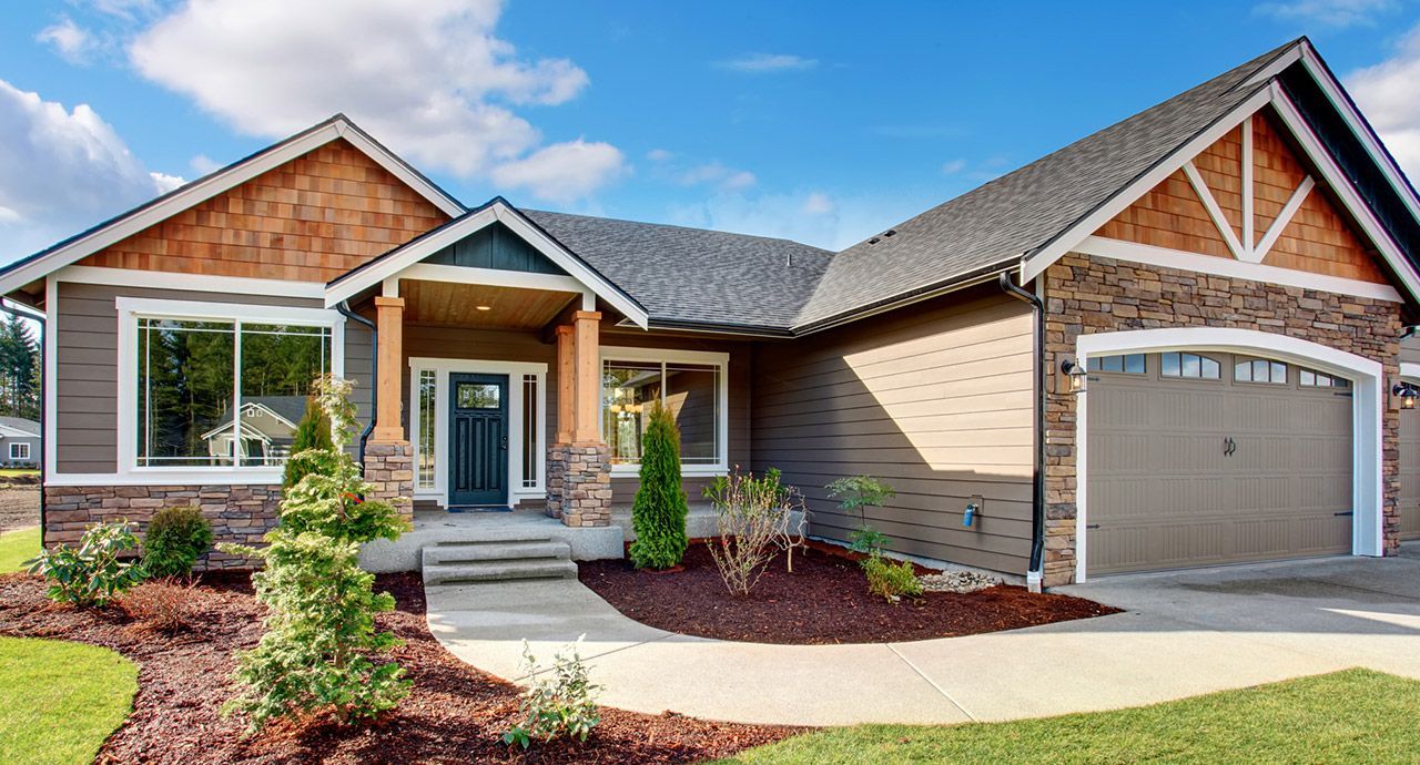 Brown and tan craftsman-style house with blue door and attached garage under a blue sky.