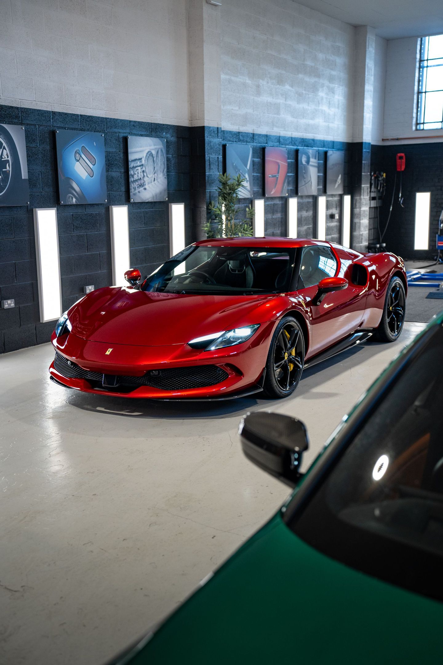A red sports car is parked in a garage next to a green car.