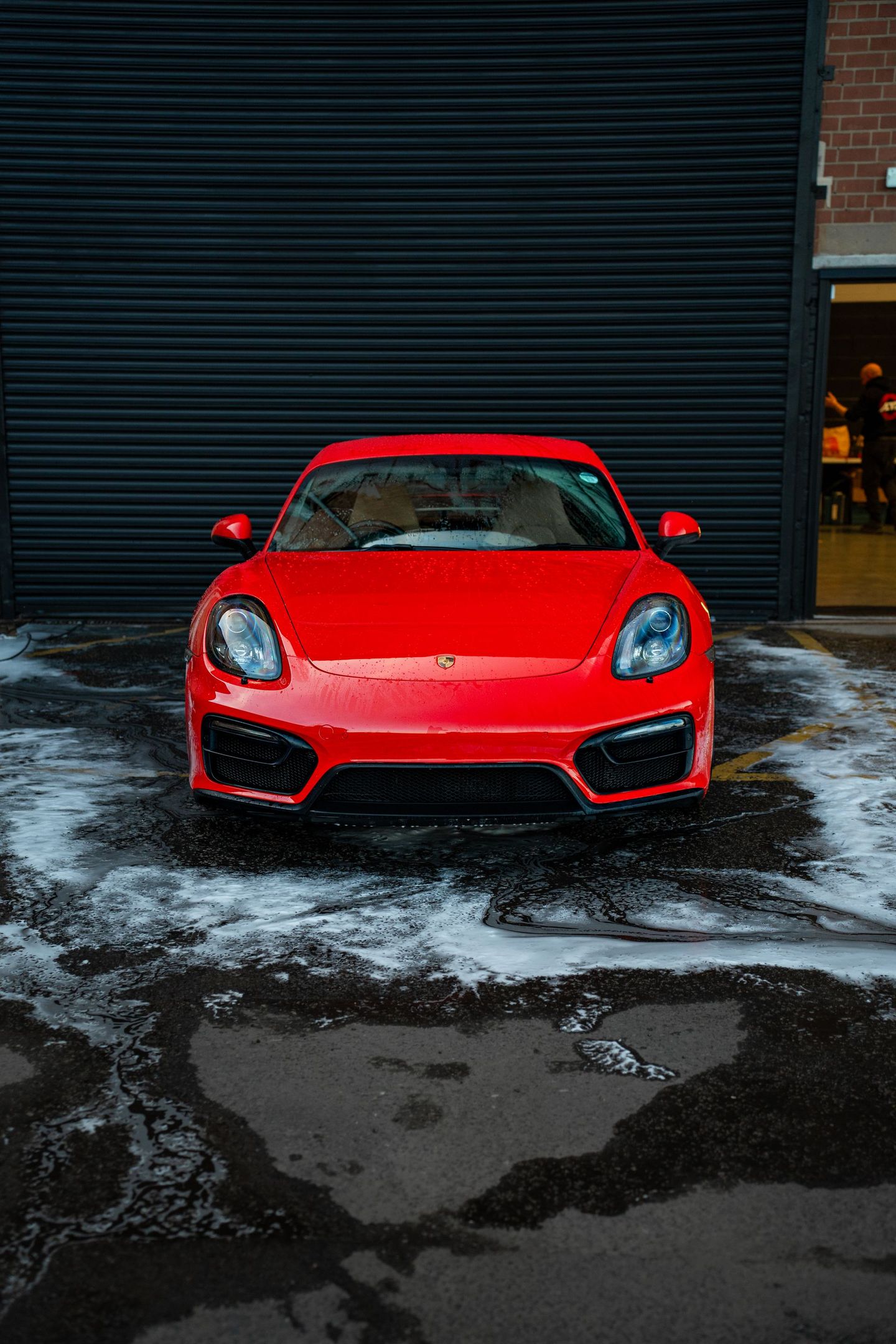 A red sports car is parked in front of a garage door.