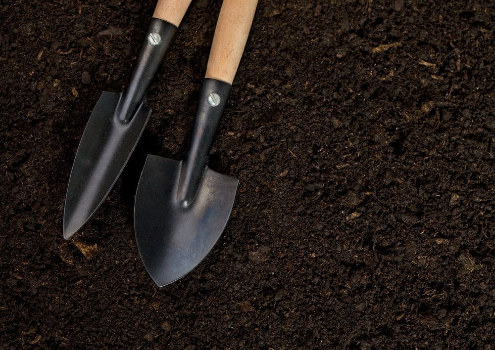 Two Gardening Trowels in Dark Brown Soil — Laurieton Landscape Supplies In Harrington, NSW