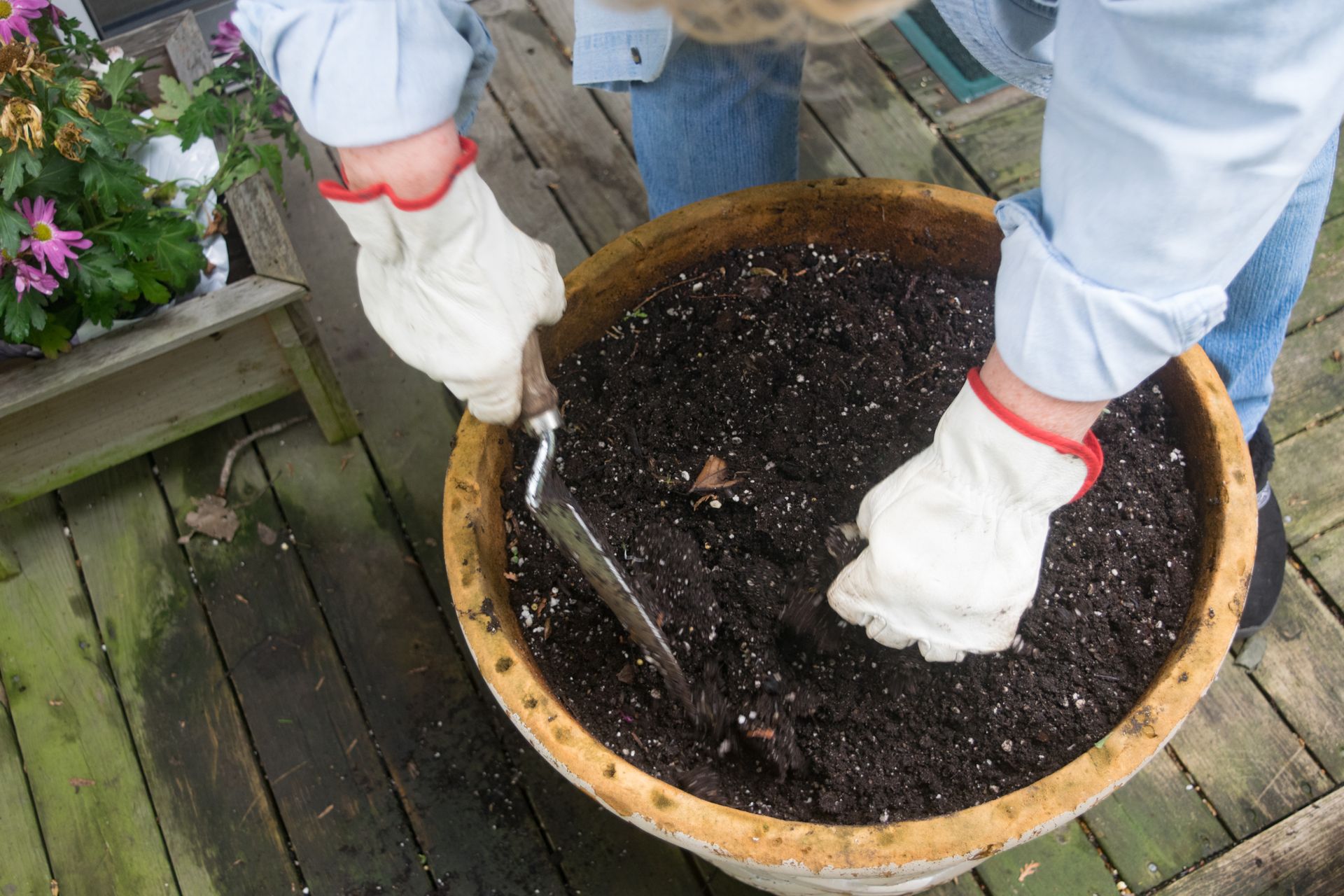 Person in Gloves Planting in a Large Pot on a Wooden Deck — Laurieton Landscape Supplies In Bonny Hills, NSW