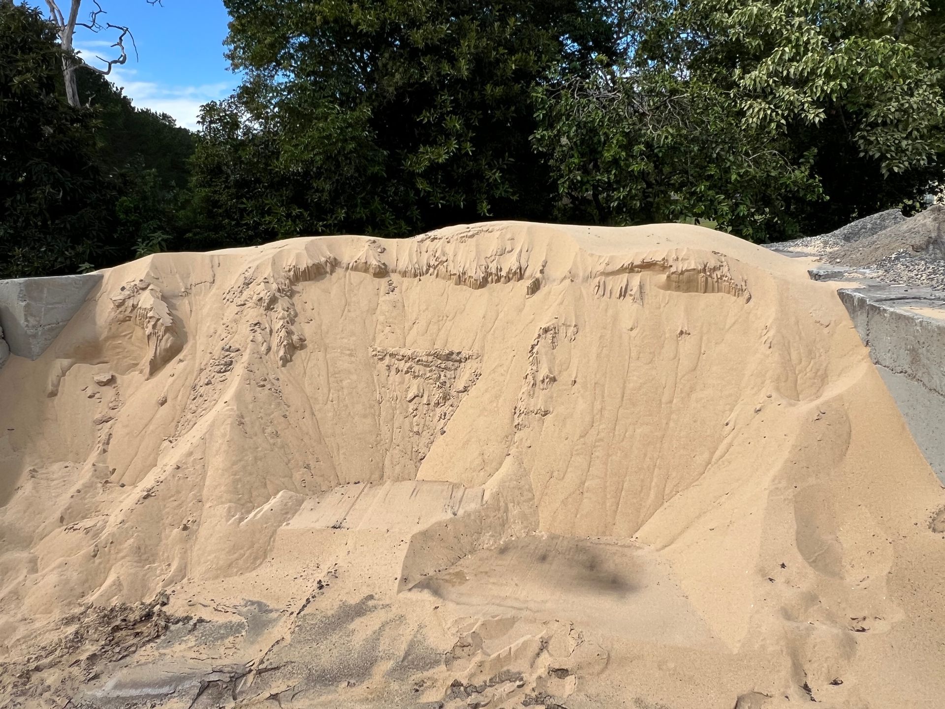 A large pile of light-tan construction sand sits outdoors against a backdrop of trees — Laurieton Landscape Supplies In Bonny Hills, NSW