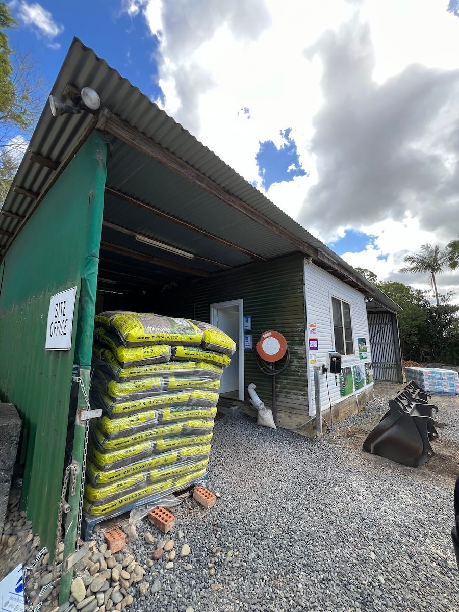 A stack of yellow product bags sits outside a shed with a green metal wall — Laurieton Landscape Supplies In Kew, NSW