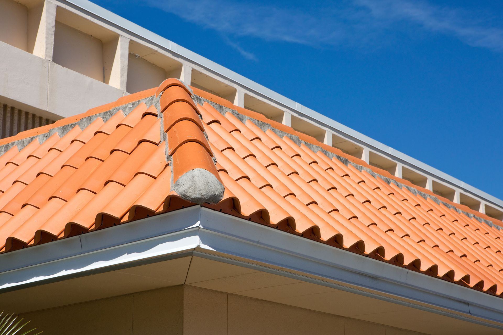 Orange clay tile roof with a gray ridge cap and white trim under a blue sky