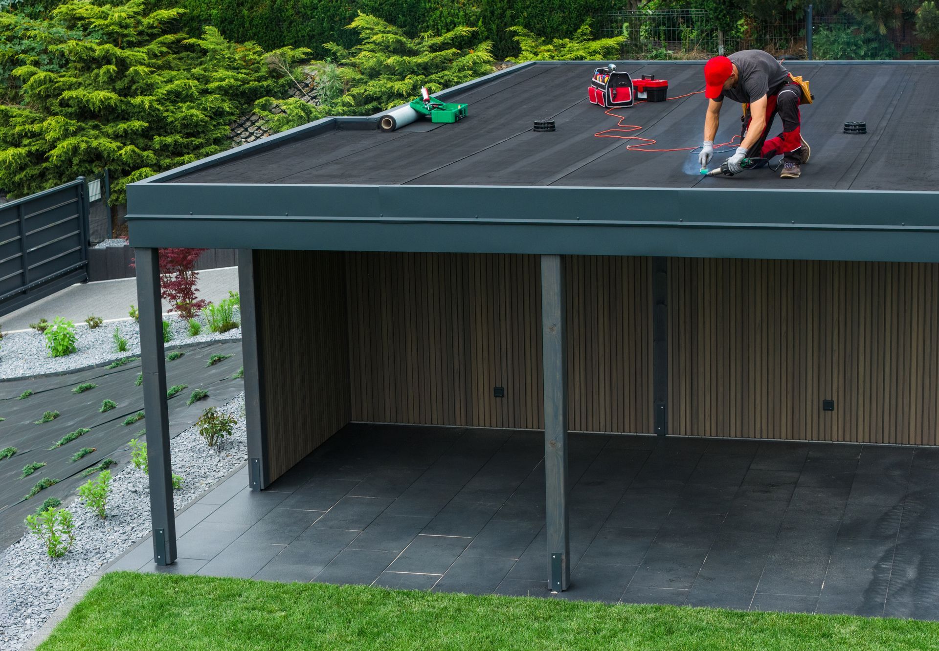 Workers installing equipment on a rooftop over a covered patio, with trees and grass below.