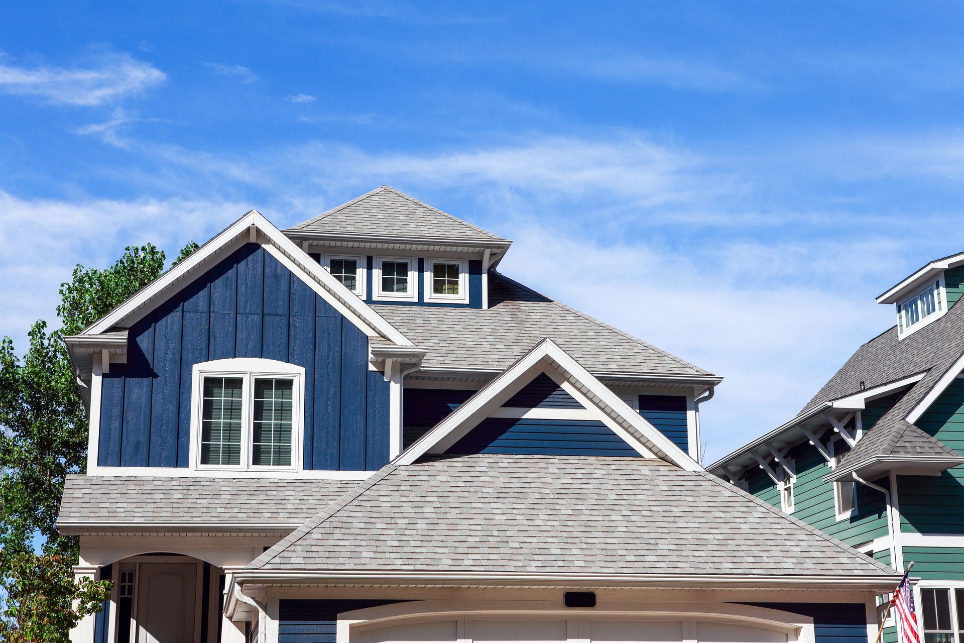 Blue two-story house with gray shingle roof and white trim under a bright blue sky