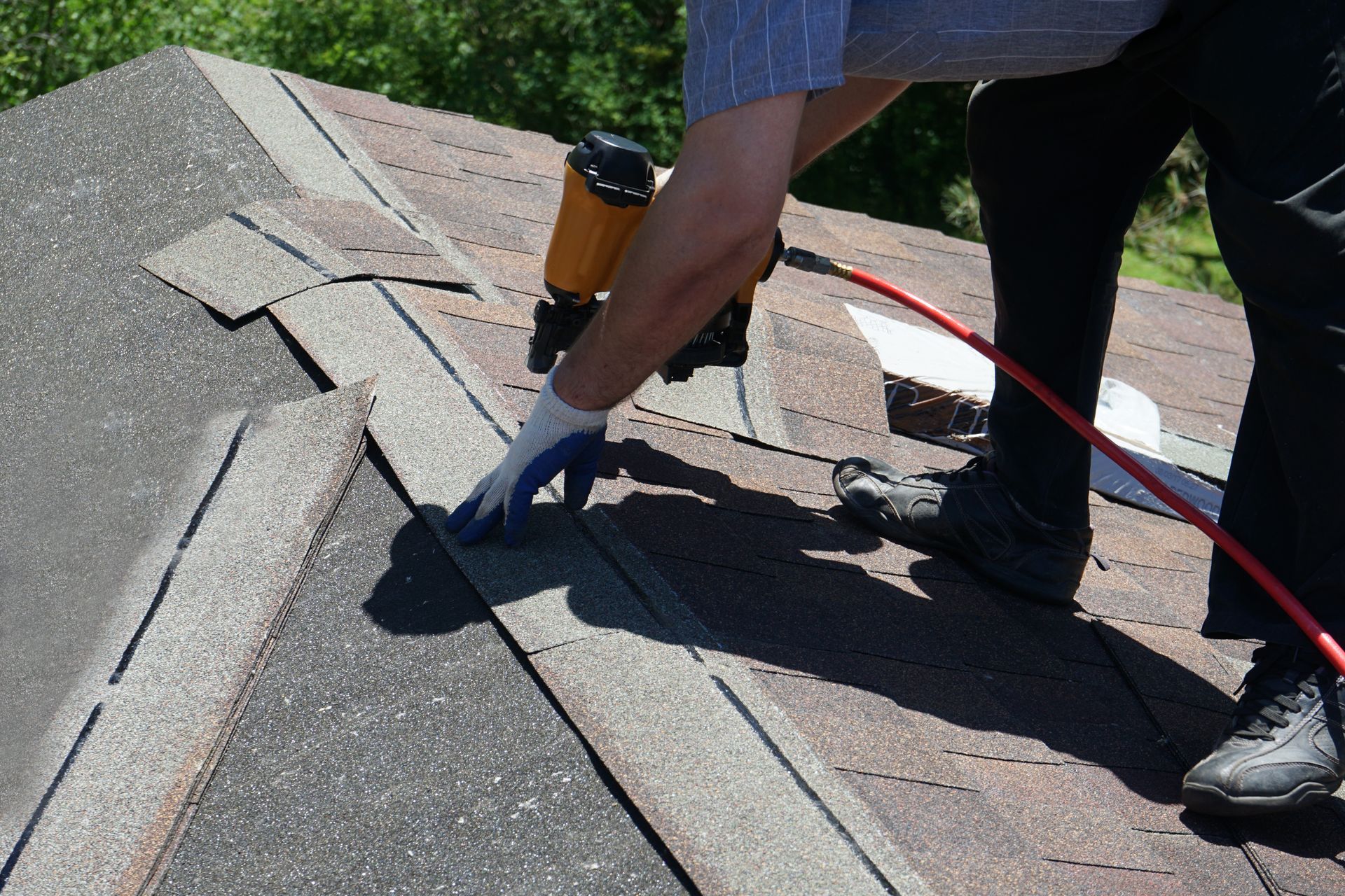 Roofing worker nailing shingles on a sloped roof with a pneumatic nail gun