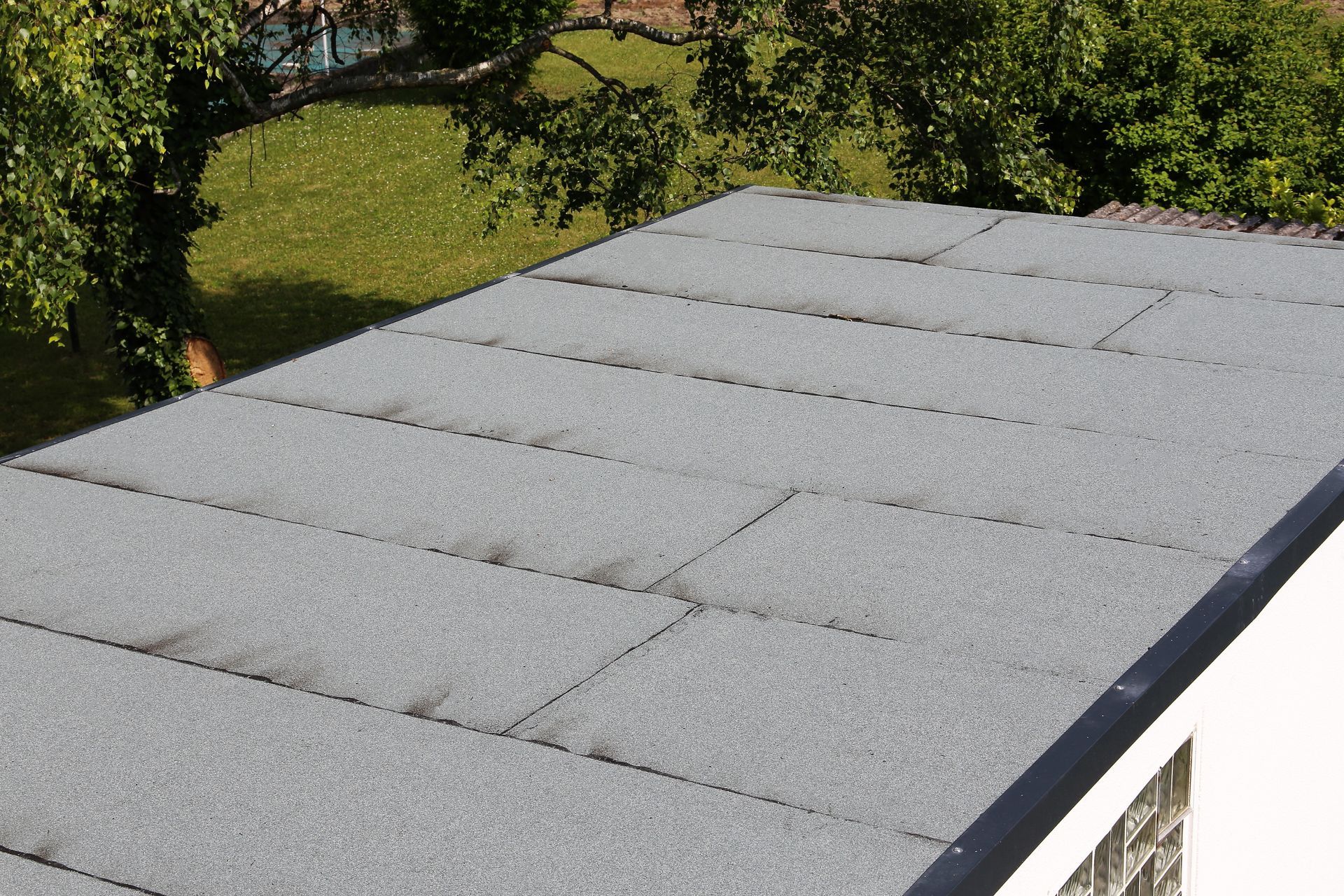 Flat gray rooftop with a white edge, seen beside green trees and grass.