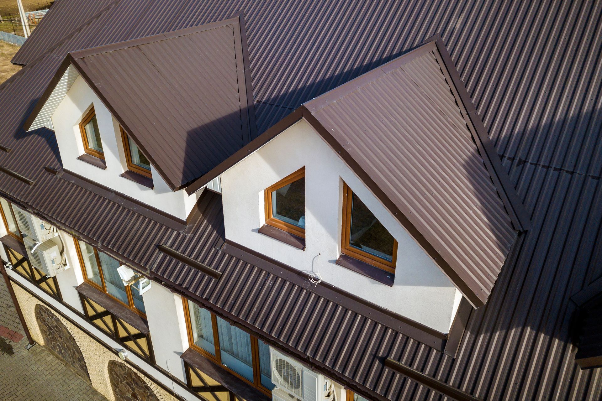Aerial view of a house roof with brown shingles, white dormer walls, and multiple windows.