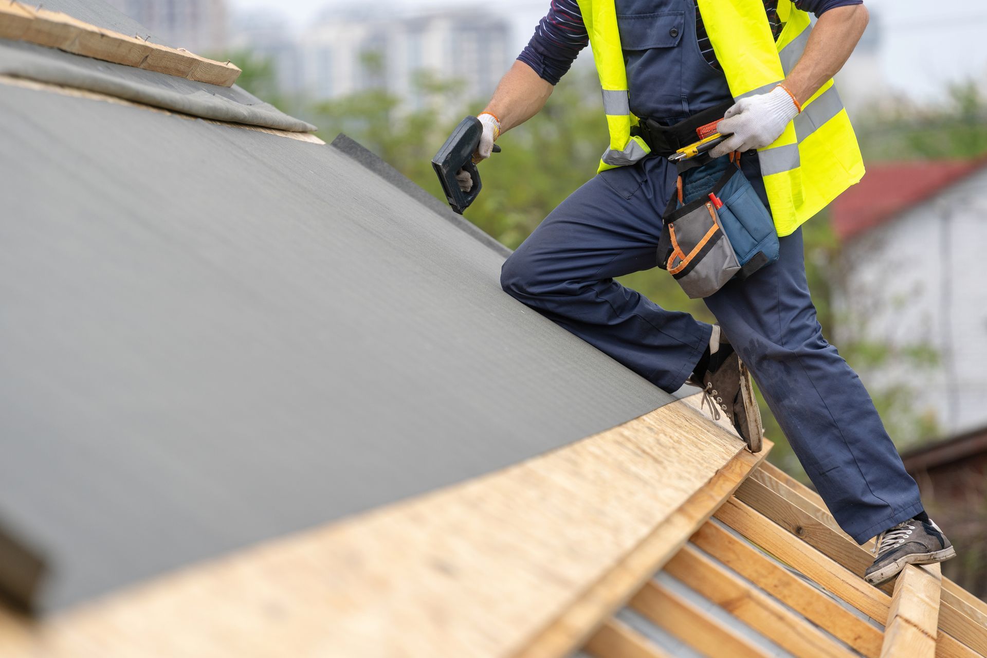 Worker in a yellow safety vest installing roofing on a sloped roof.
