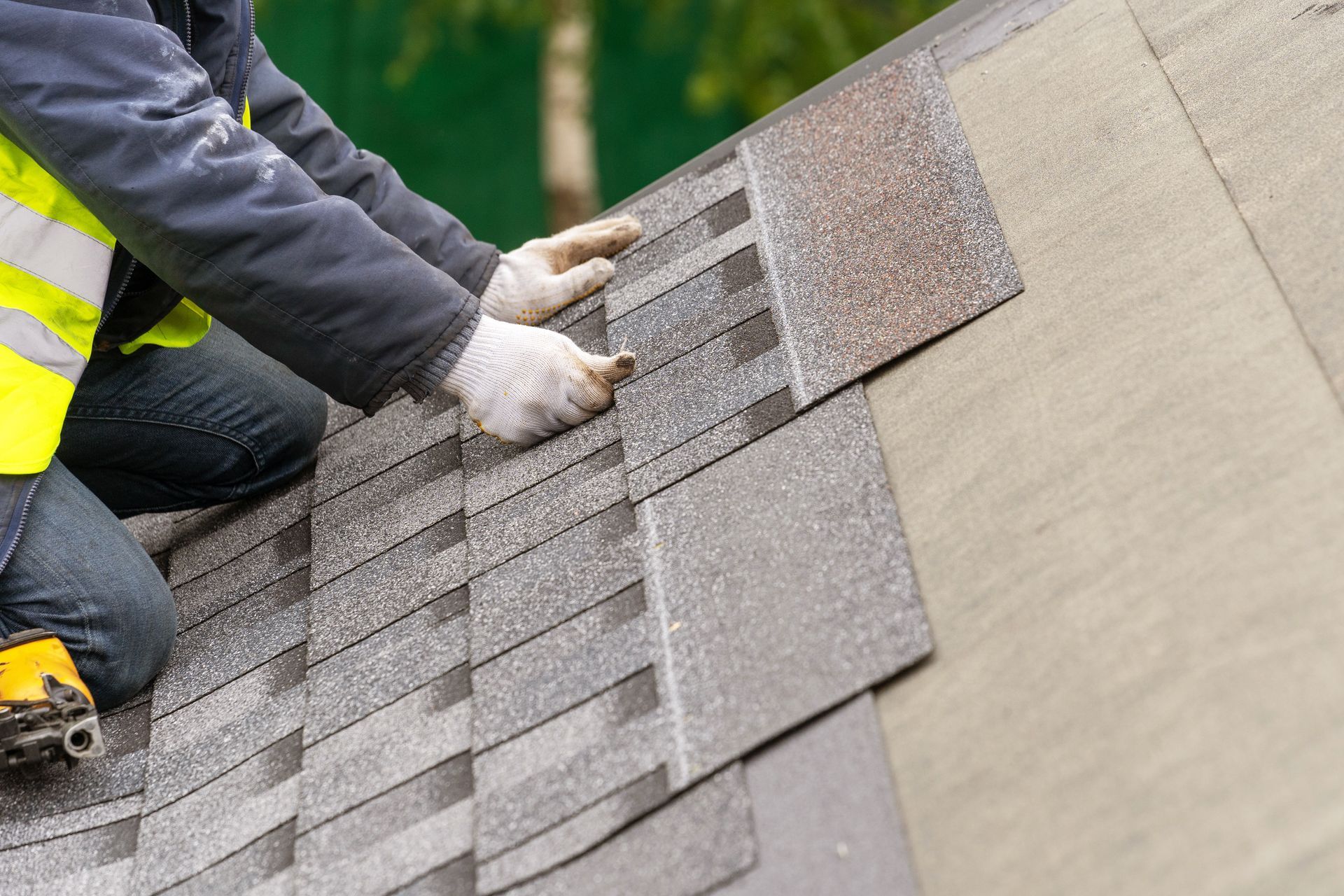 Worker installing gray roof shingles on a sloped roof