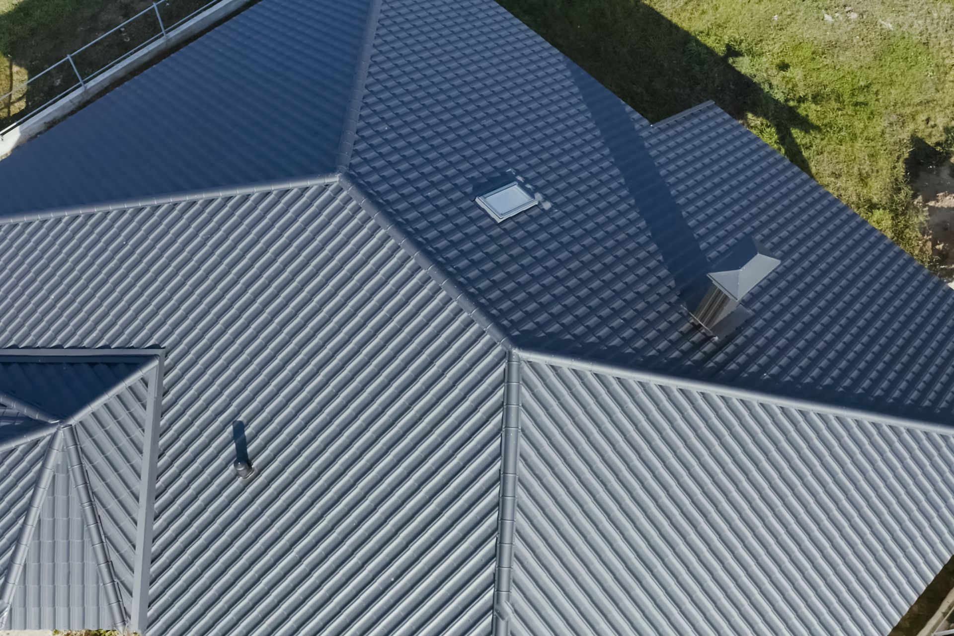 Aerial view of a gray metal roof with vents, skylights, and surrounding greenery