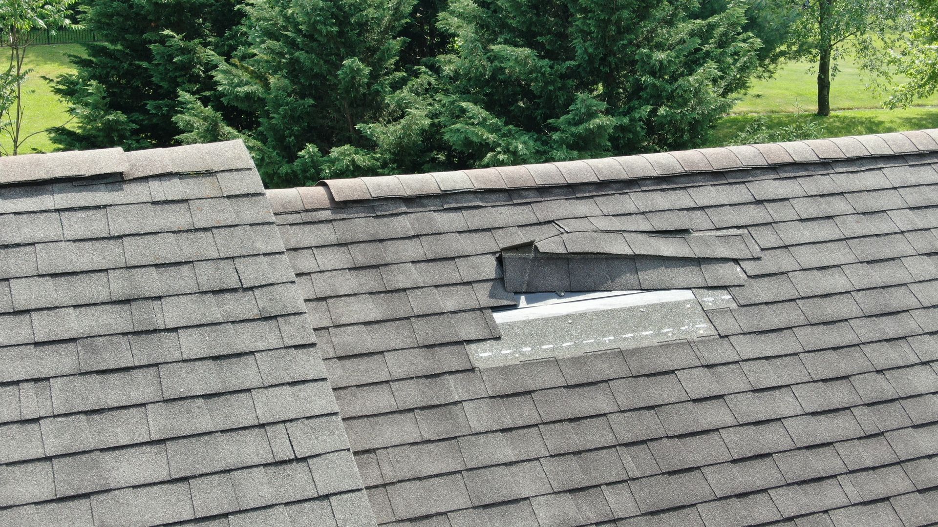 Roof with a damaged shingle area and exposed black underlayment near the ridge.