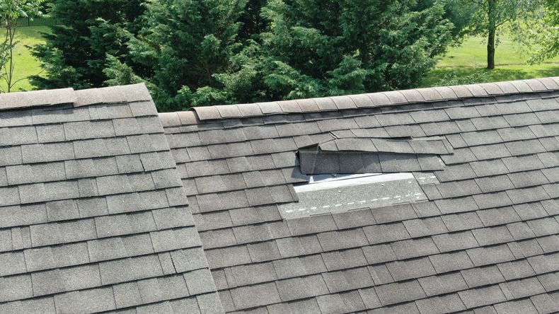 Damaged gray shingle roof with a hole and exposed patch near the ridge.