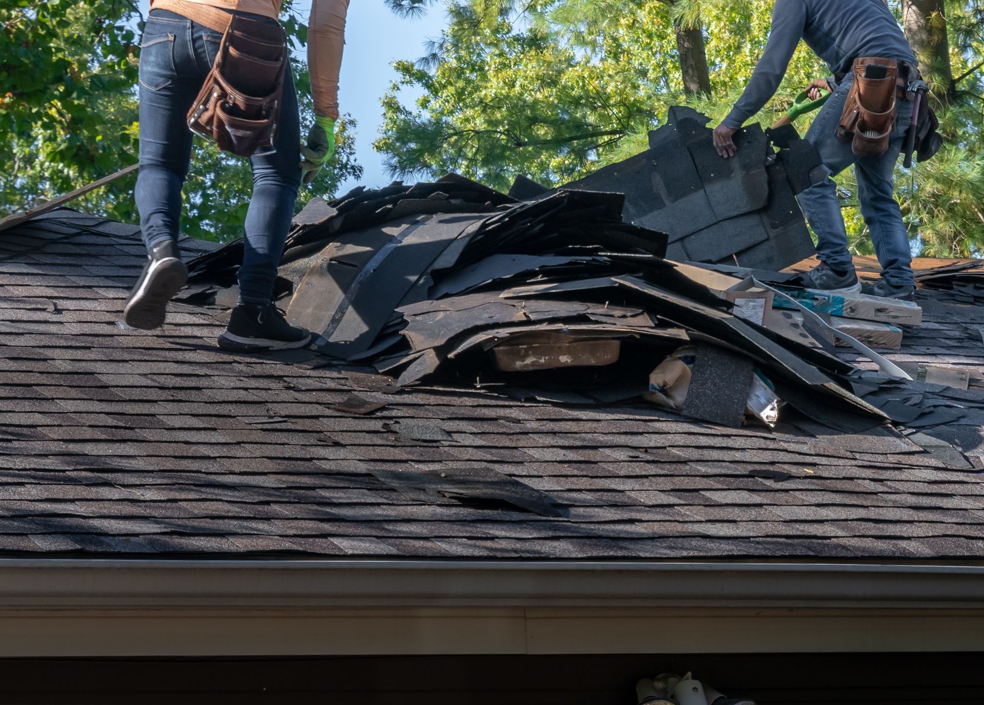 Workers removing damaged shingles from a roof after storm damage