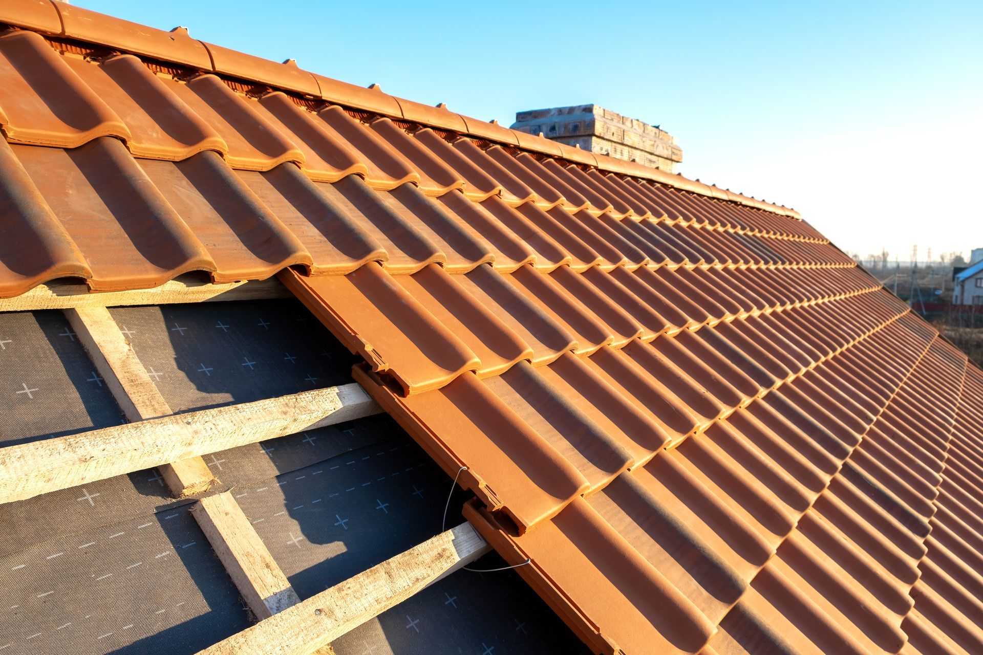 Roof under construction with terracotta tiles and exposed wooden battens under a blue sky