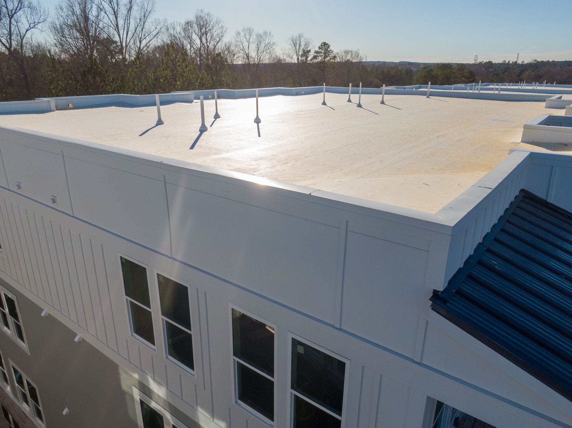 Flat white rooftop with vents on a building under a clear sky, viewed from above
