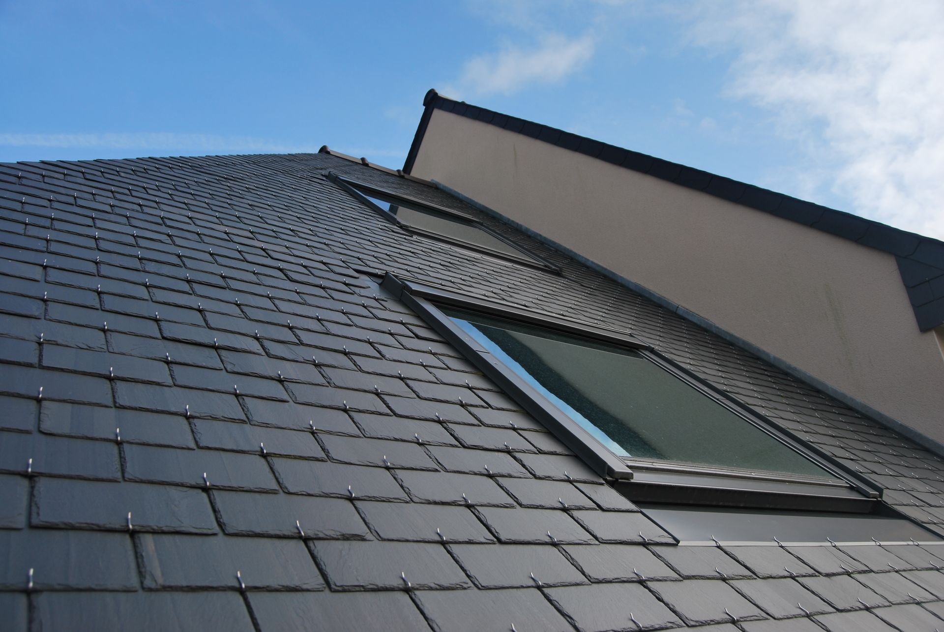 Dark tiled roof with a skylight against a blue sky