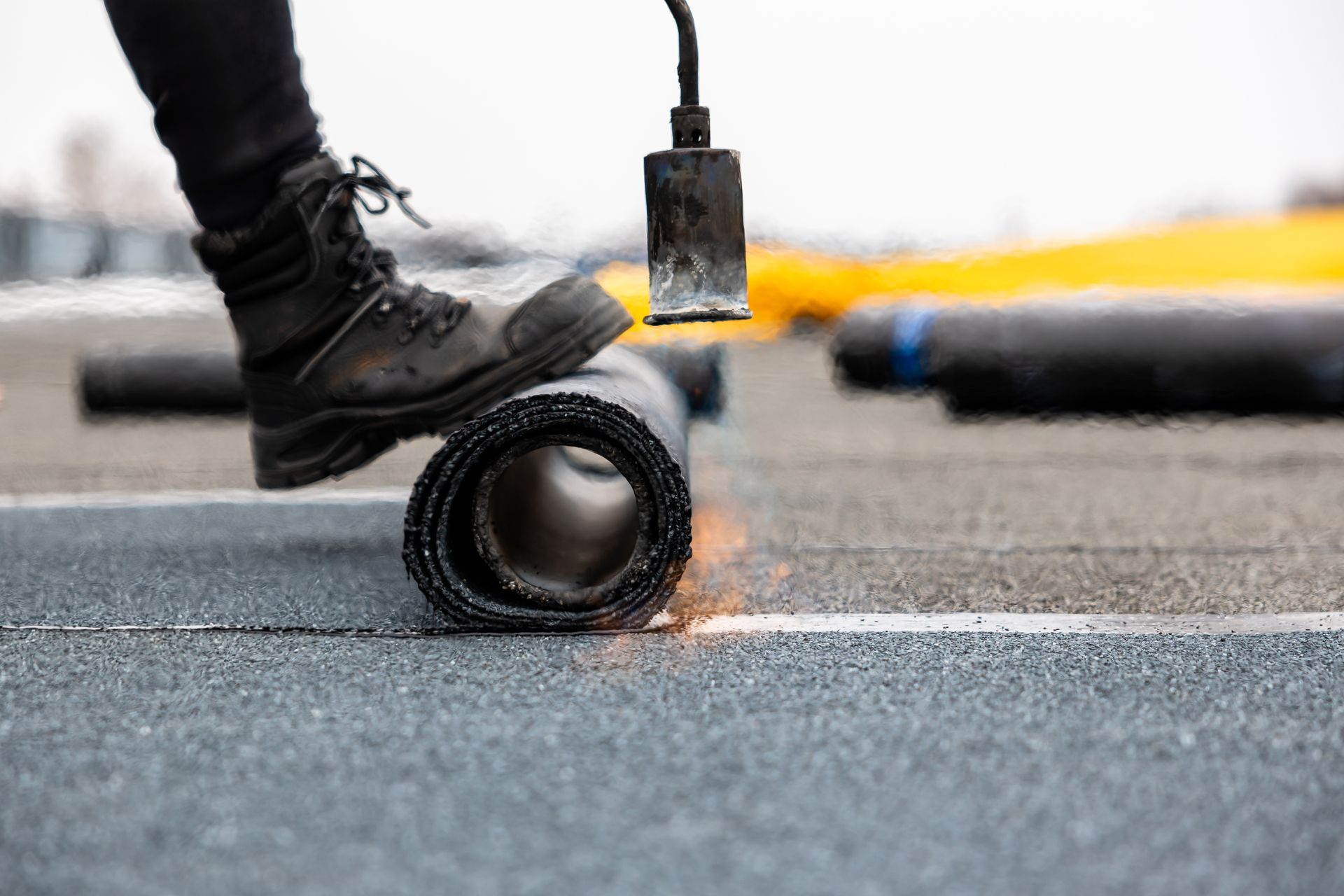 Worker using a pneumatic tool to crush a tire on asphalt, with a boot nearby and sparks flying