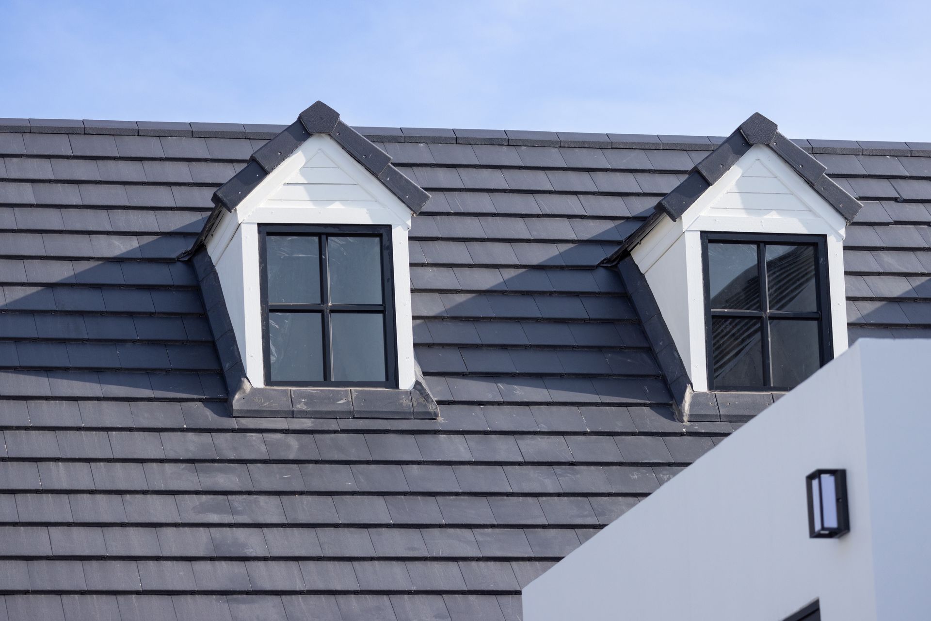 Gray tiled roof with two dormer windows on a white house under a blue sky