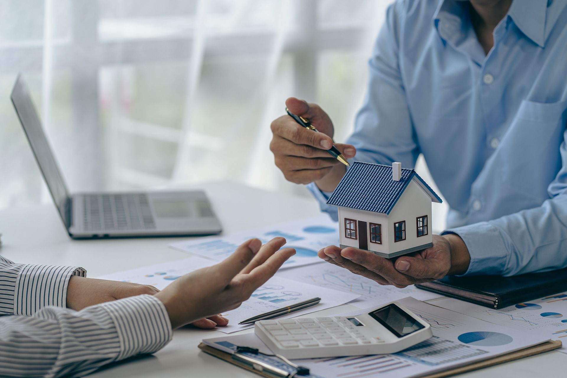 A man is holding a model house in his hands while talking to a woman