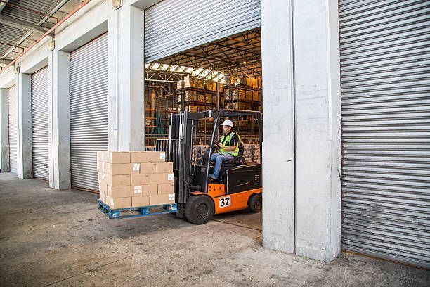 A forklift moves boxes through an open commercial garage door.