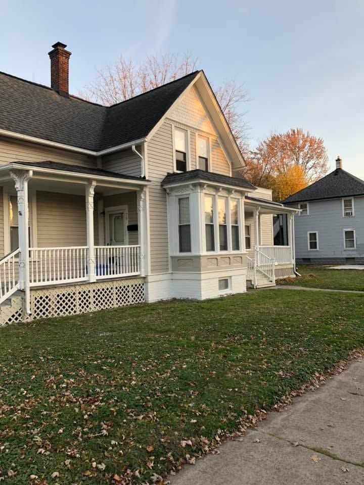 White house with porch and front lawn beside a sidewalk at sunset