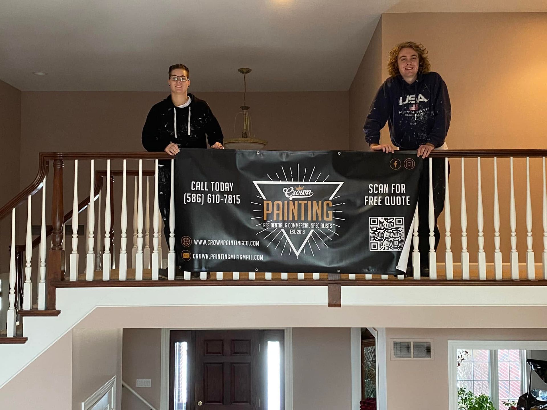 Two people stand on an upstairs balcony holding a black banner with a triangle logo.