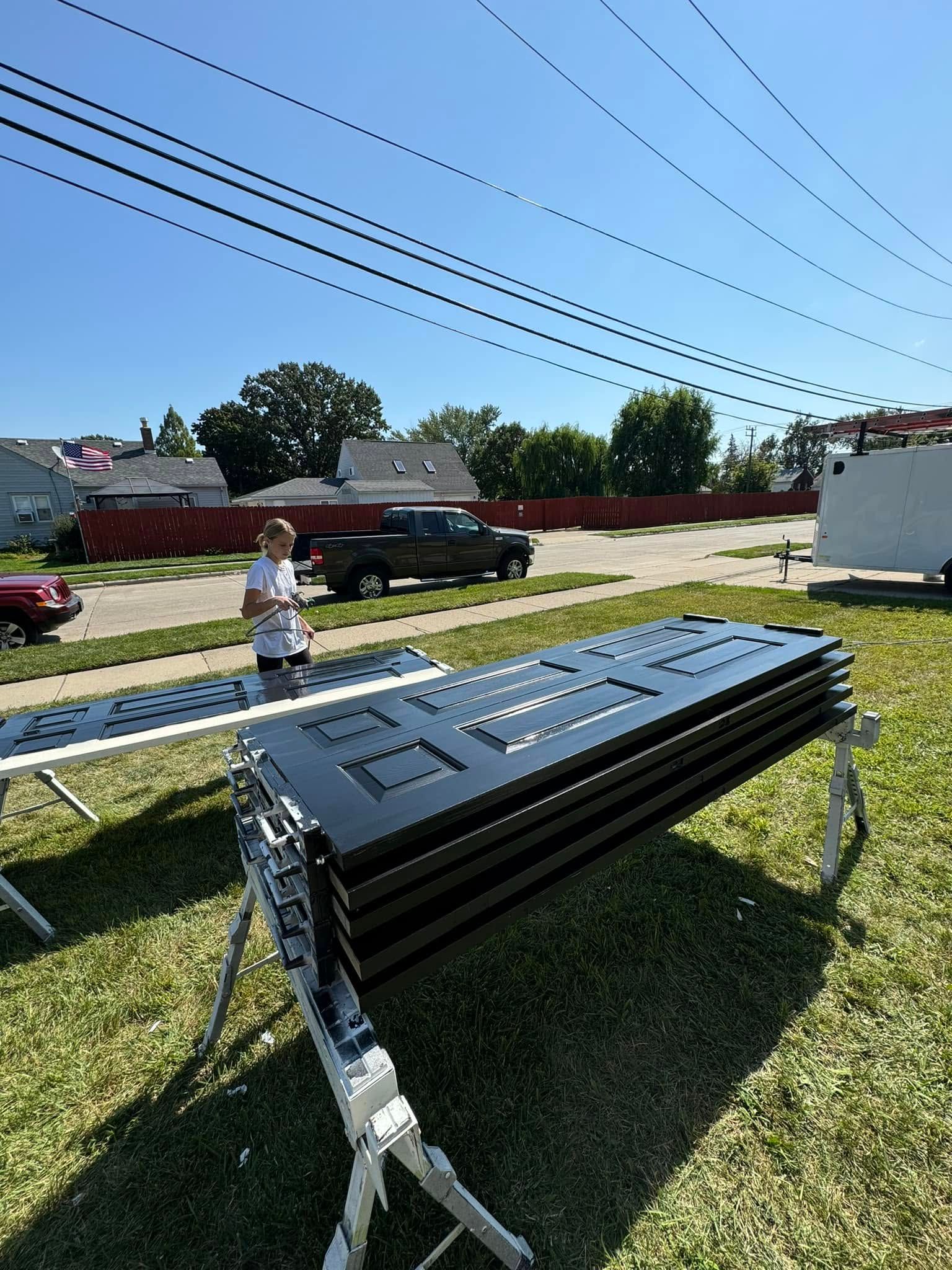 Stacks of black school desks on a grassy roadside with a child and parked cars in the background