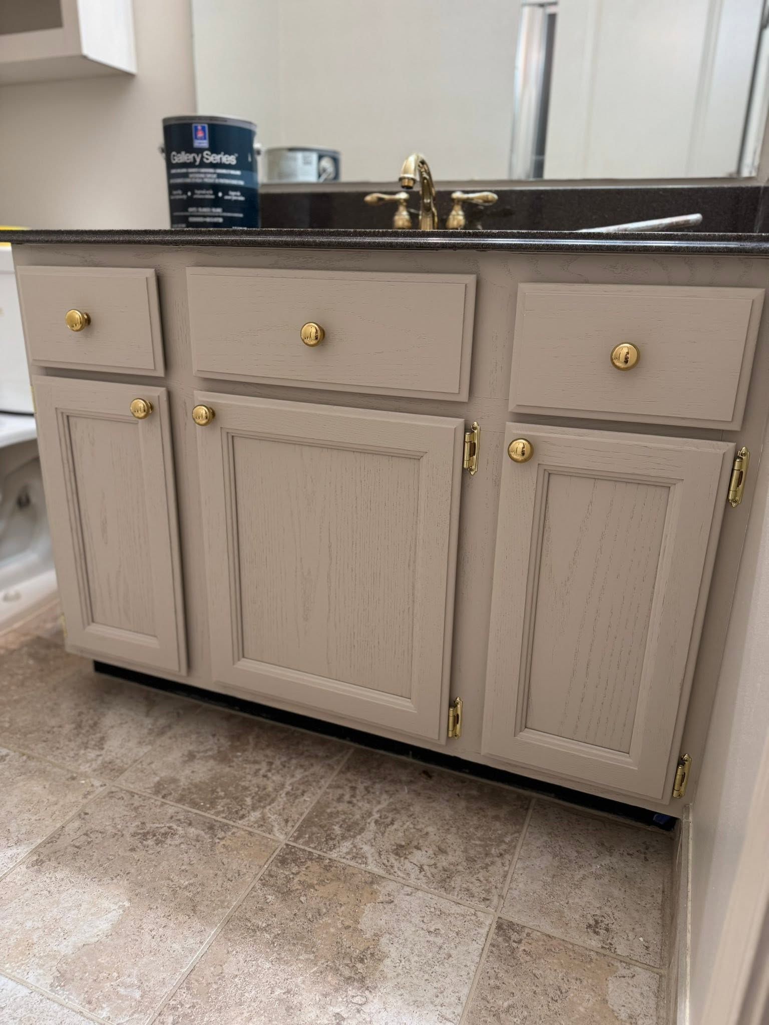Beige bathroom vanity with gold knobs, white countertop, faucet, and sink against a mirror.