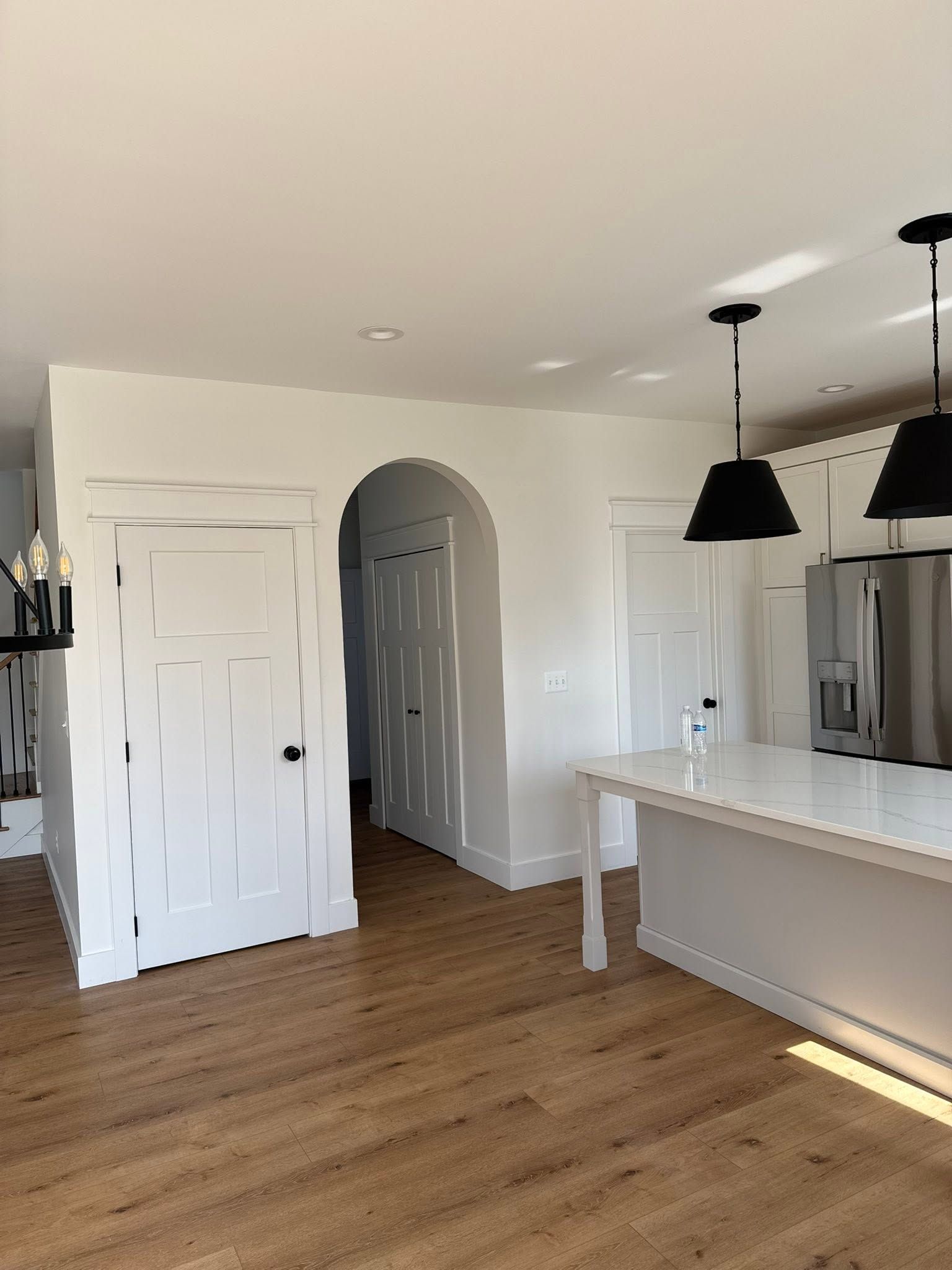 Bright empty kitchen with wood floors, white cabinets, gray island, and black pendant lights