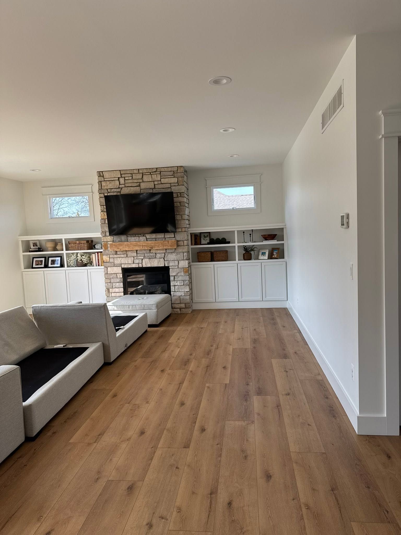 Modern living room with gray sectional, wood floors, and a stone fireplace with TV above it