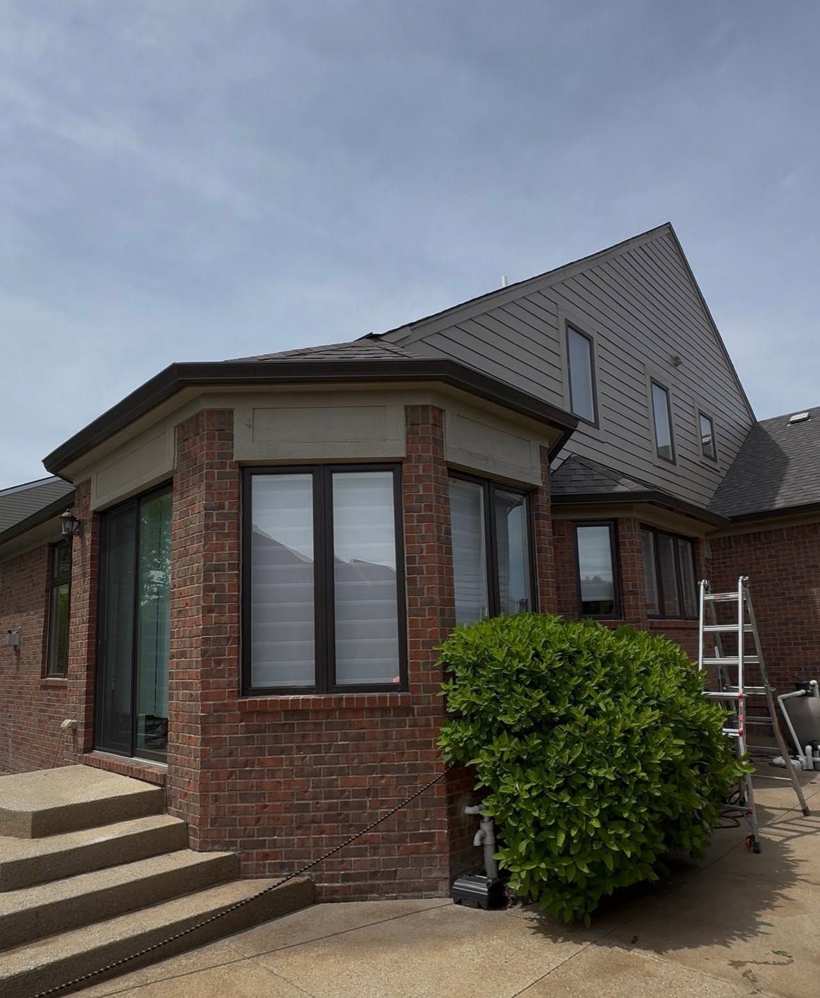 Brick house exterior with steps, shrubs, and a ladder near the roof