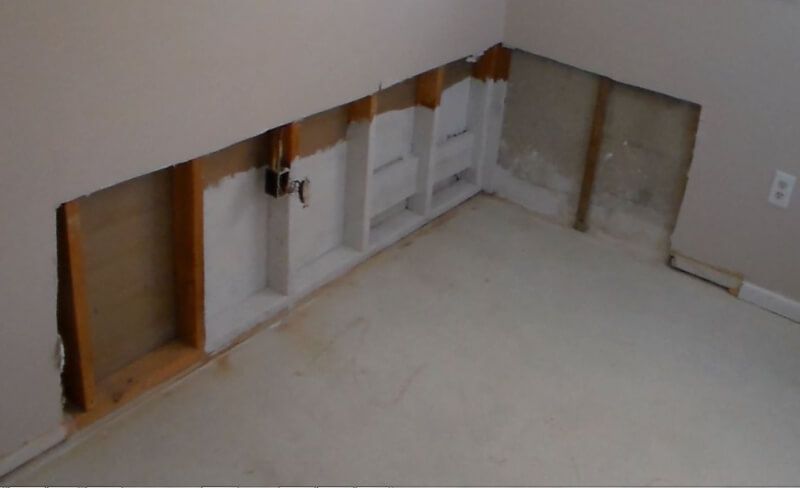 Unfinished basement wall with exposed studs, wiring, and white paneling beneath a sloped ceiling.