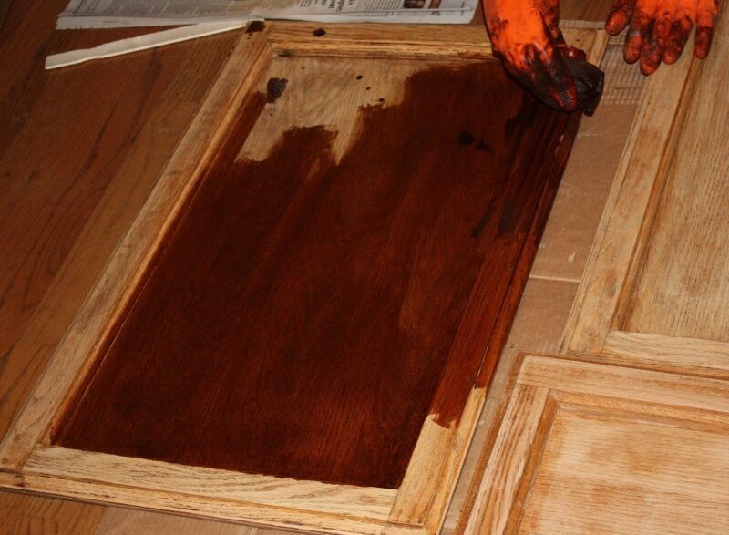Hands staining a wooden panel with dark brown finish inside a workshop