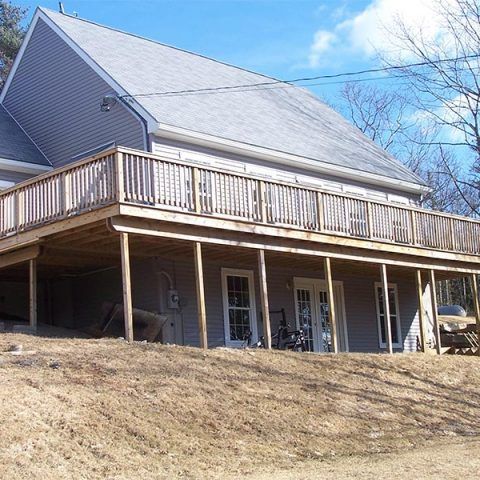 House with large wooden deck on a sloped hillside under a blue sky