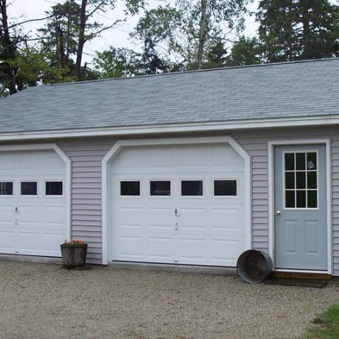 Two white garage doors and a gray side door on a beige house with a gravel driveway