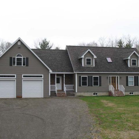 Suburban duplex with two garage doors, gray siding, and small front porches under an overcast sky