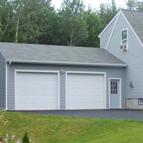 Two-car white garage beside a gray house with a black driveway and green lawn