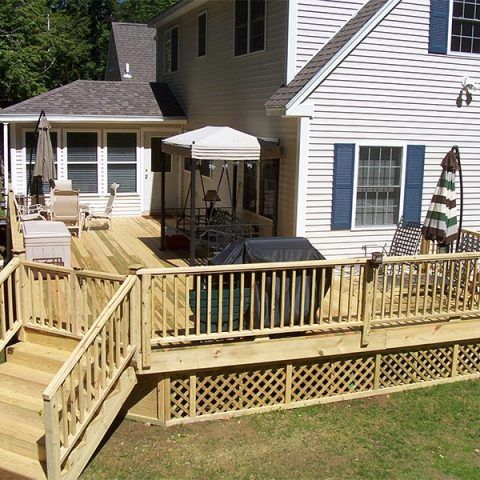 Back deck with wooden ramp, railing, and patio furniture beside a white house