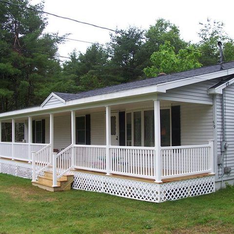 White single-story house with a covered porch, white railing, and steps in a wooded yard